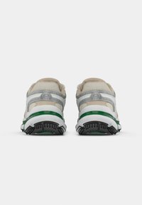 Ett par beige och grå sneakers med gröna detaljer, sedd bakifrån mot en enkel vit bakgrund.