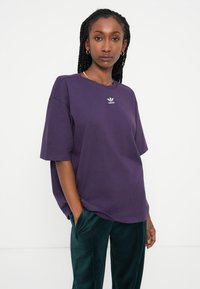 Fialové oversized tričko s krátkymi rukávmi, s malým bielym logom Adidas na hrudi. Hladký bavlnený materiál s voľným strihom.