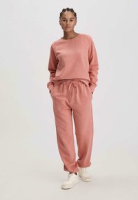 Felpa in pile rosa con scollo rotondo e maniche lunghe, abbinata a pantaloni jogger coordinati con vita elasticizzata e tasche laterali.