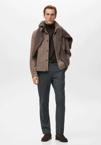 Brązowy wełniany płaszcz na ciemnym golfie, w połączeniu z szarymi, dopasowanymi spodniami. Wąski krój z guzikami oraz brązowe zamszowe buty.