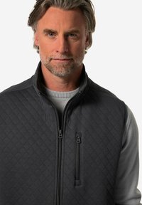 Quiltad svart väst med dragkedjeförsedda framfickor, hög krage och grå långärmad baslager. Texturerad tyg och strömlinjeformat stil.