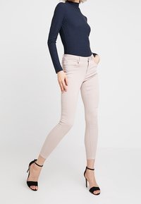 Jeans ajustados de color rosa claro con bolsillos frontales, combinados con una camiseta de manga larga de canalé en color navy y sandalias negras de tacón alto.