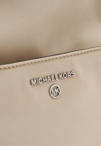 Borsa in tessuto beige con logo e simbolo argentati "MICHAEL KORS". Texture liscia con bordi cuciti, design minimalista.