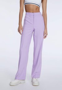Lila wijde broek gemaakt van rekbaar materiaal, met een hoge taille en een strakke voorkant. Gecombineerd met witte chunky sneakers.
