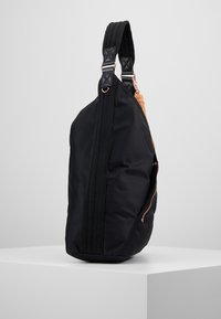 Black nylon bag with a structured shape, featuring a dual strap, rose gold hardware, and an exterior zipper pocket for storage.