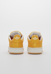 Yellow suede sneakers with white accents and rubber soles, featuring a padded collar and a textured logo on the heel.