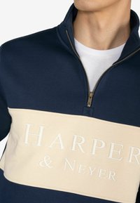 Granatowa bluza z zamkiem błyskawicznym z kremowym poziomym panelem, z wyraźnym napisem "HARPER & NEYER". Miękki materiał i widoczne kontrastowe tekstury.