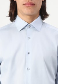 Light blue button-up shirt made of smooth fabric, featuring a spread collar and five buttons with dark circular accents.