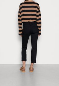Black jeans with a slim fit and cropped length paired with a striped brown and black long-sleeve top. Tan sandals complete the outfit.