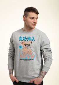 Sudadera gris con un gráfico de un oso de dibujos animados con gafas de sol, texto en negrita azul y rosa, y puños y dobladillo acanalados.