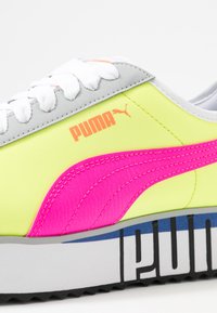 Obuv s neonově žlutým svrškem, růžovými akcenty a šedou patou, bílými tkaničkami a výraznou černobílou pruhovanou podrážkou.