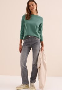 Groene longsleeve shirt, grijze spijkerbroek en beige jas. Lichte sneakers met gestructureerde accenten. Eenvoudige, relaxte pasvorm en casual stijl.