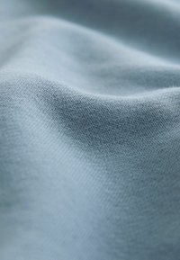 Tessuto blu chiaro con una consistenza morbida, caratterizzato da un fine motivo a maglia. La superficie appare liscia con leggere ondulazioni.