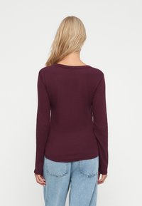 Langærmet, dyb burgunder top i ribbet stof, med en bred halsudskæring og tætsiddende silhuet, parret med lyseblå denim jeans.