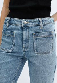 Los jeans de mezclilla azul claro presentan una cintura alta, un diseño clásico de cinco bolsillos, costuras en contraste y un cierre de botón metálico en el frente.