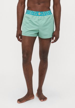 Green swim shorts with a turquoise patterned waistband featuring a geometric design and logo. Made of lightweight fabric, knee-length cut.