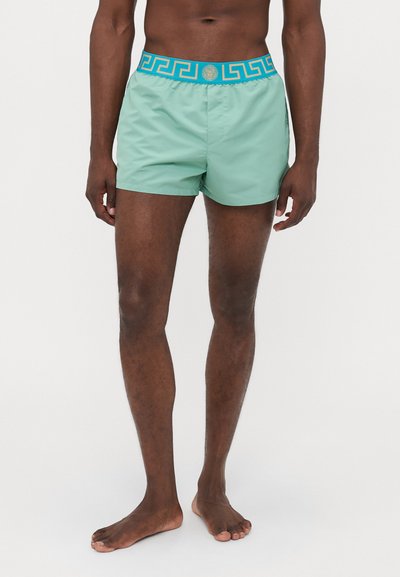 Pantaloni da bagno verdi con una cintura a motivo turchese caratterizzata da un design geometrico e logo. Realizzati in tessuto leggero, taglio fino al ginocchio.