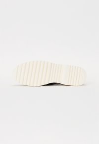 Semelle de chaussure avec fond en caoutchouc blanc strié, présenté à plat sur un fond blanc, mettant en valeur le motif de la bande de roulement et la texture.