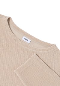 Pull en beige à côtes avec un col rond et une étiquette avec "Cecil". Le tissu présente une apparence texturée et tricotée.