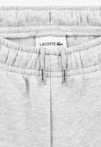 Grå bomullssweatpants med elastisk midje, snor og en Lacoste-label med krokodillelogo. Jevn tekstur.