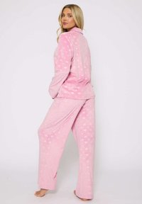 Set di pigiama in pile rosa composto da una maglietta a maniche lunghe con colletto e pantaloni, decorati con un motivo a cuori. Texture morbida e accogliente.