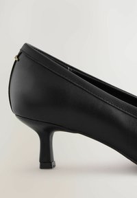 Scarpa nera con tacco alto realizzata in materiale sintetico liscio, con punta appuntita e tacco sottile con base quadrata. Accento dorato sul retro.
