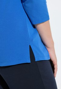 Niebieska bawełniana koszula z krótkimi rękawami, z rozcięciami po bokach na dole, zestawiona z czarnymi legginsami. Gładka tekstura i luźny krój.