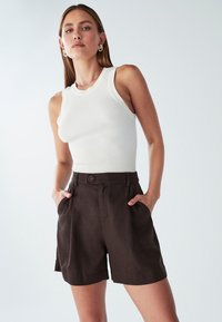 Witte geribde tanktop gecombineerd met donkerbruine op maat gemaakte shorts met zijzakken en een knoopsluiting. Gladstof textuur, casual pasvorm.