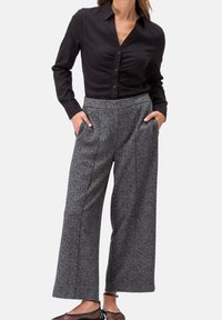 Chemise noire à boutons, à manches longues, associée à un pantalon large à carreaux gris avec poches latérales et tissu texturé.