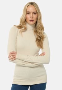 Beige Rollkragenpullover aus weichem Stoff, mit langen Ärmeln und figurbetonter Passform, sowie einem gerippten Saum und Bündchen.