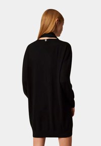 Vestito nero a maglia con maniche lunghe, vestibilità comoda, scollo tondo e un dettaglio logo discreto sul retro. Texture liscia e design minimalista.