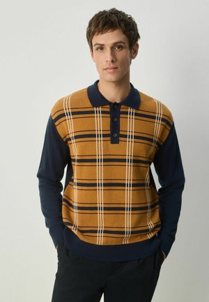 Strik polo sweater kombinerer orange-brun med marineblå ærmer. Har vandrette striber og tre knapper ved kraven. Blød tekstur.