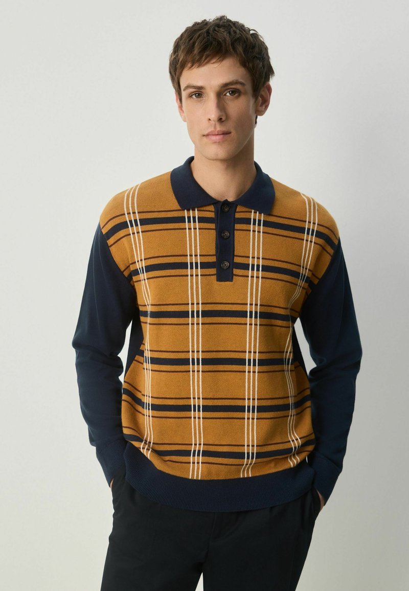 Strik polo sweater kombinerer orange-brun med marineblå ærmer. Har vandrette striber og tre knapper ved kraven. Blød tekstur.