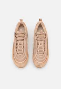 Beige sneakers med en mjuk, lager-på-lager design och rund tå, texturerade detaljer och gummisula. Snörningarna är ordentligt säkrade.