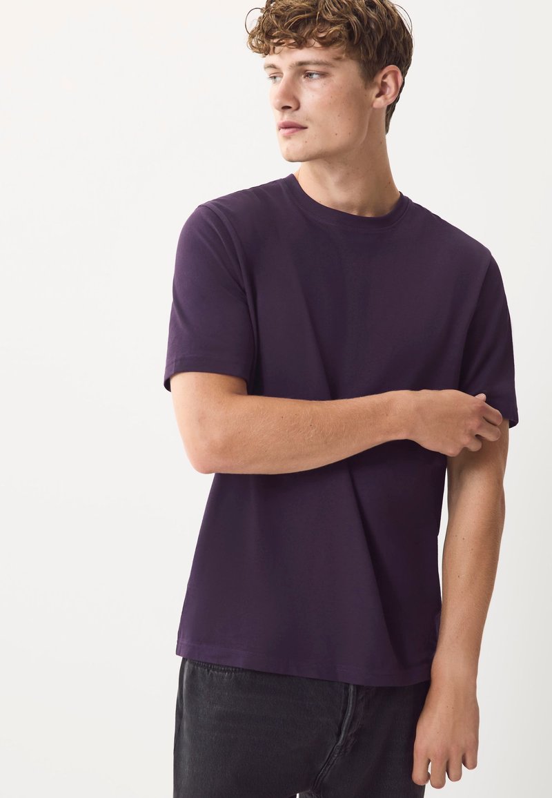 Lilla bomulds-t-shirt med rund halsudskæring og korte ærmer, med en afslappet pasform og glat tekstur, kombineret med mørke jeans.