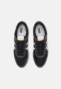 Un par de zapatillas Asics en negro y gris con rayas de logo blancas, cordones negros y plantillas "EZFOAM", vistas desde arriba sobre un fondo blanco.