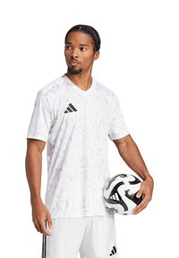 Witte voetbalsjersey met triangulaire patronen, korte mouwen en V-hals. Zwart Adidas-logo. De speler houdt een zwart-wit voetbal vast.