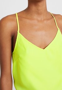 Top senza maniche di un giallo neon con scollatura a V, realizzato in tessuto liscio. Presenta spalline sottili e una vestibilità comoda, con un dettaglio di cucitura minimale.