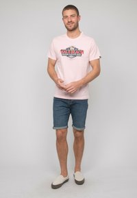 T-shirt rose à manches courtes avec un graphique "MAUL BEACH", associé à un short en denim roulé et des chaussures légères à enfiler. Design simple, look décontracté.