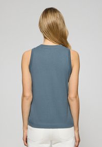 Bez rękawów, prążkowany top w stonowanym niebieskim kolorze, z okrągłym dekoltem i dopasowanym krojem, połączony z kremowymi spodniami.