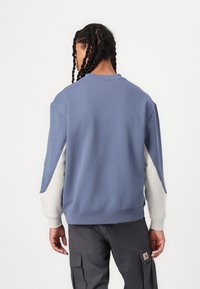 Sudadera azul con detalles en gris claro, corte relajado, cuello redondo y mangas raglán. Presenta una textura suave y un dobladillo de punto acanalado.