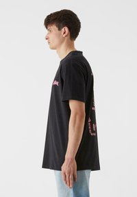 Must musta t-särk lühikeste varrukatega, ümar kaelus ja roosad graafikud ees ja taga, nähtav külgvaates.