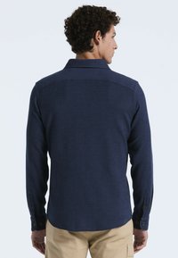 Marineblauwe blouse met lange mouwen, een kraag en knoopmanchetten, met een zachte textuur en een gebogen zoom.