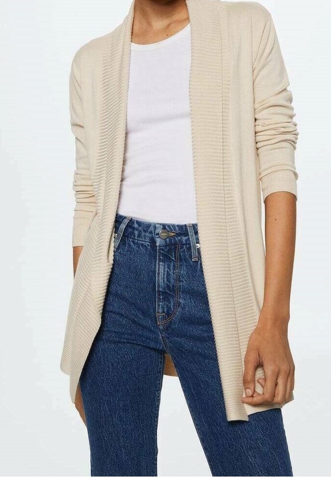 Cardigan beige à ouverture devant, porté sur un t-shirt blanc à col rond, associé à un jean en denim bleu taille haute.