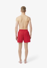 Shorts de bain rouges avec une taille élastique et une poche arrière, vus de dos, présentant un tissu lisse et léger avec une coupe décontractée.