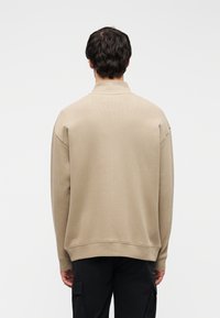 Φωτεινό μπεζ φούτερ με ψηλό γιακά, ραμμένους ώμους, ριμπ μανσέτες και τελείωμα. Λείο ύφασμα και άνετη εφαρμογή.