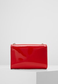 Borsa rettangolare in pelle verniciata rossa con finitura lucida, dotata di chiusura con zip superiore e dettagli di cucitura sottili lungo i bordi.