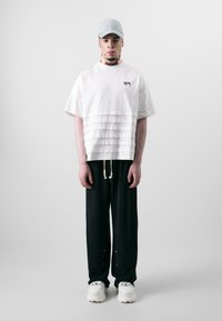 White short-sleeved t-shirt with layered texture and black drawstring pants. Complemented by a light blue cap and chunky white sneakers.