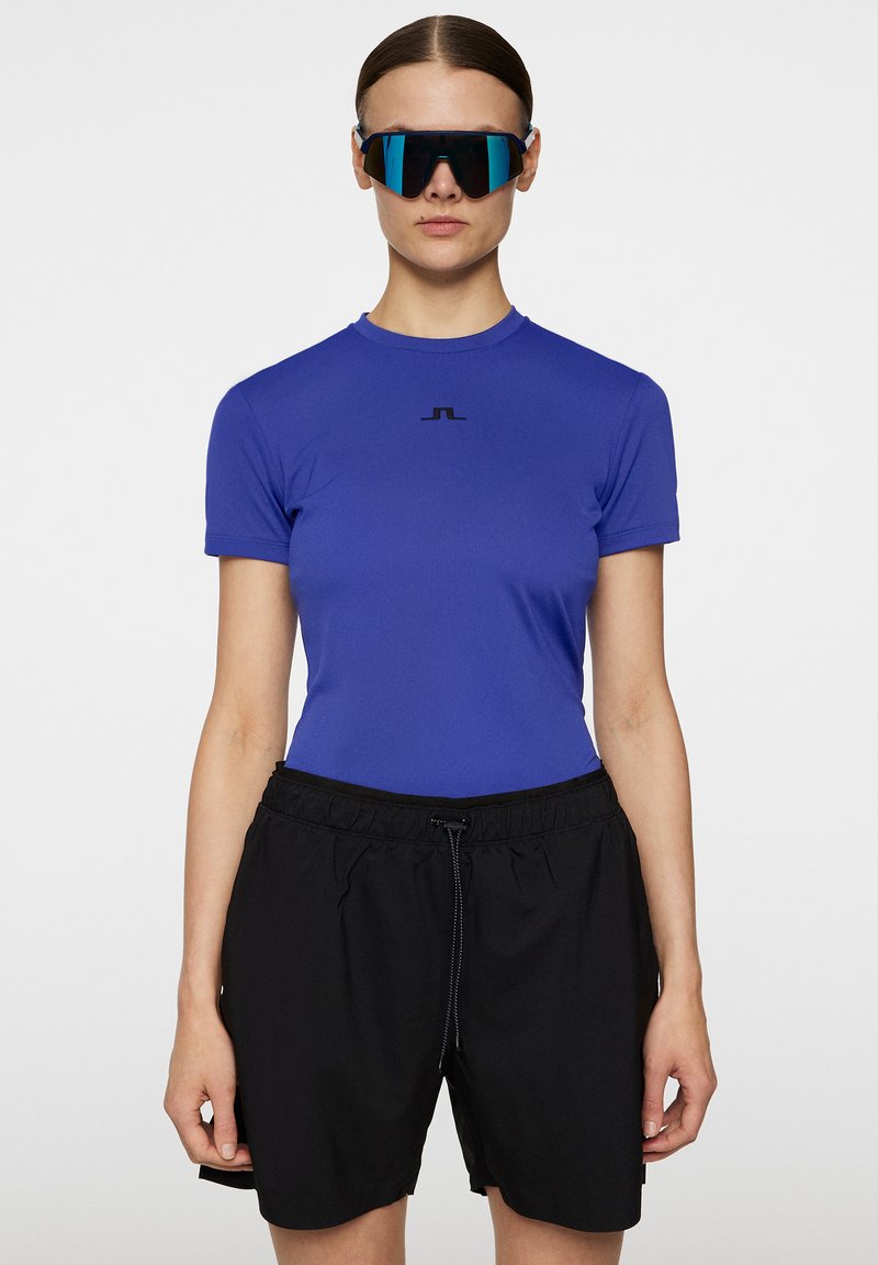 Blå, figursydd kortärmad skjorta med en svart logotyp på bröstet, tillsammans med svarta lösa shorts med elastisk midja och snörning.