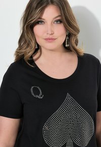 Camiseta negra con un gran diseño de espade de strass y una 'Q' de strass en el lado izquierdo del pecho. Tela suave con un escote redondeado.